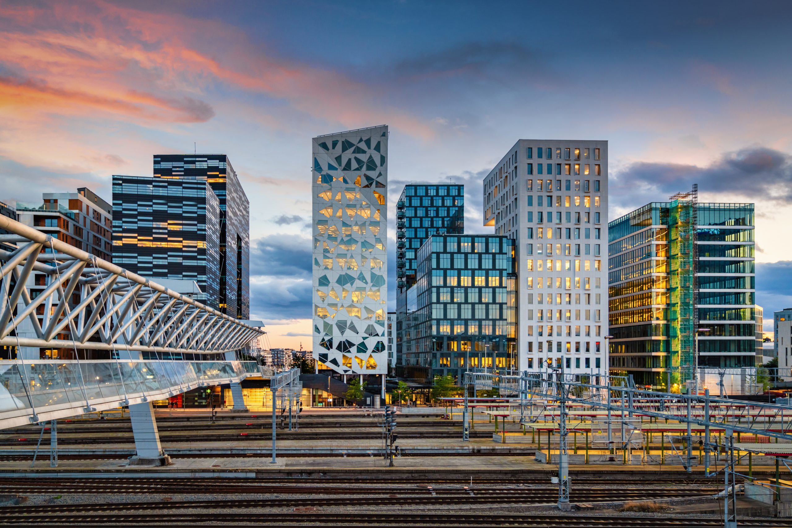 Sunset twilight over downtown Oslo, the capital city of Norway. Pedestrian Bridge over rails of central railway station on the left. Illuminated modern Business Buildings and Skyscaper Cityscape in late Summer at Dusk. Oslo, Norway, Scandinavia