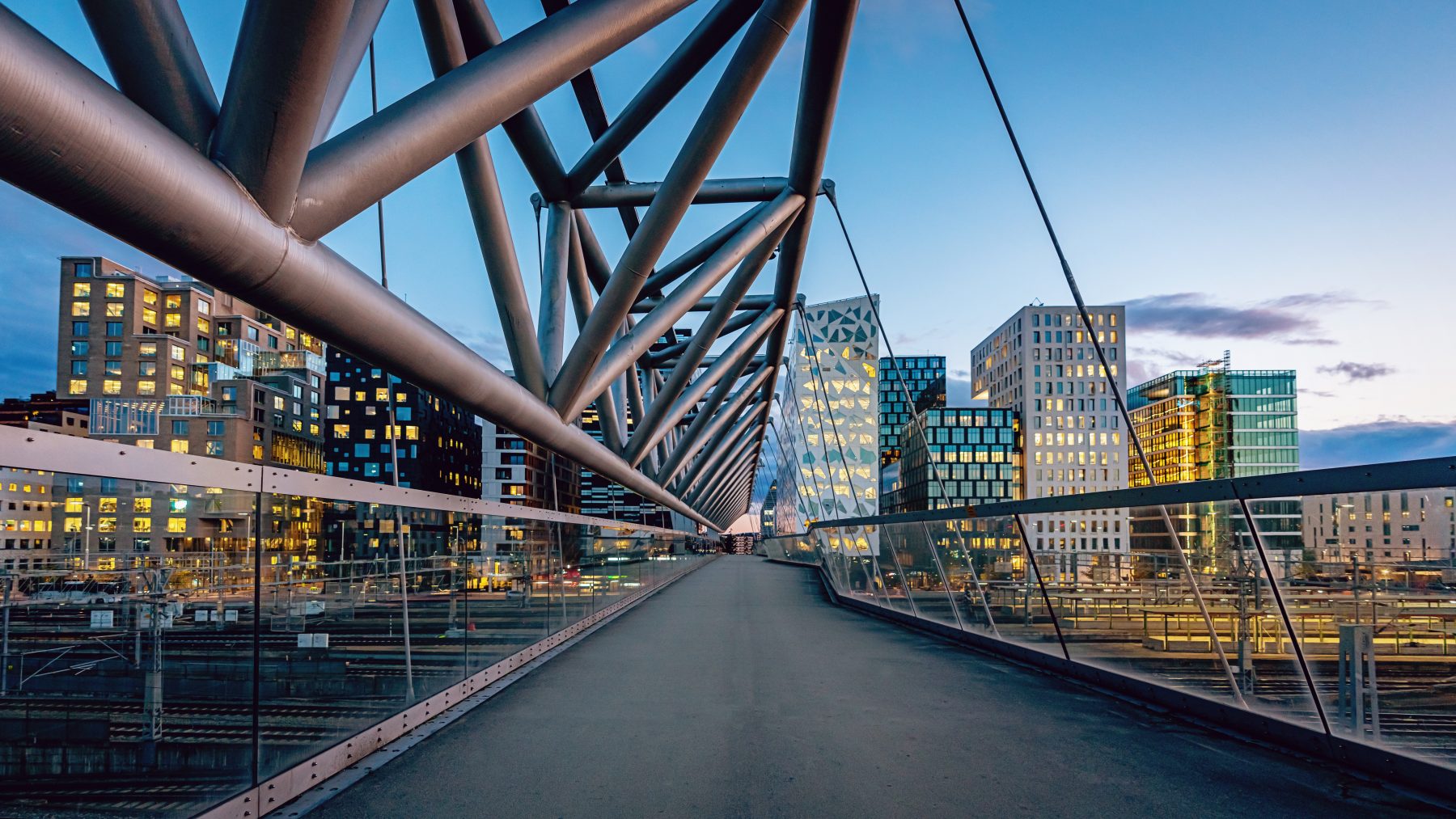 Beautiful twilight over downtown Oslo, the capital city of Norway at Pedestrian Bridge over rails of central railway station. Illuminated modern buildings and skyscapers. Cityscape from elevated walkway in late summer. Oslo, Norway, Scandinavia